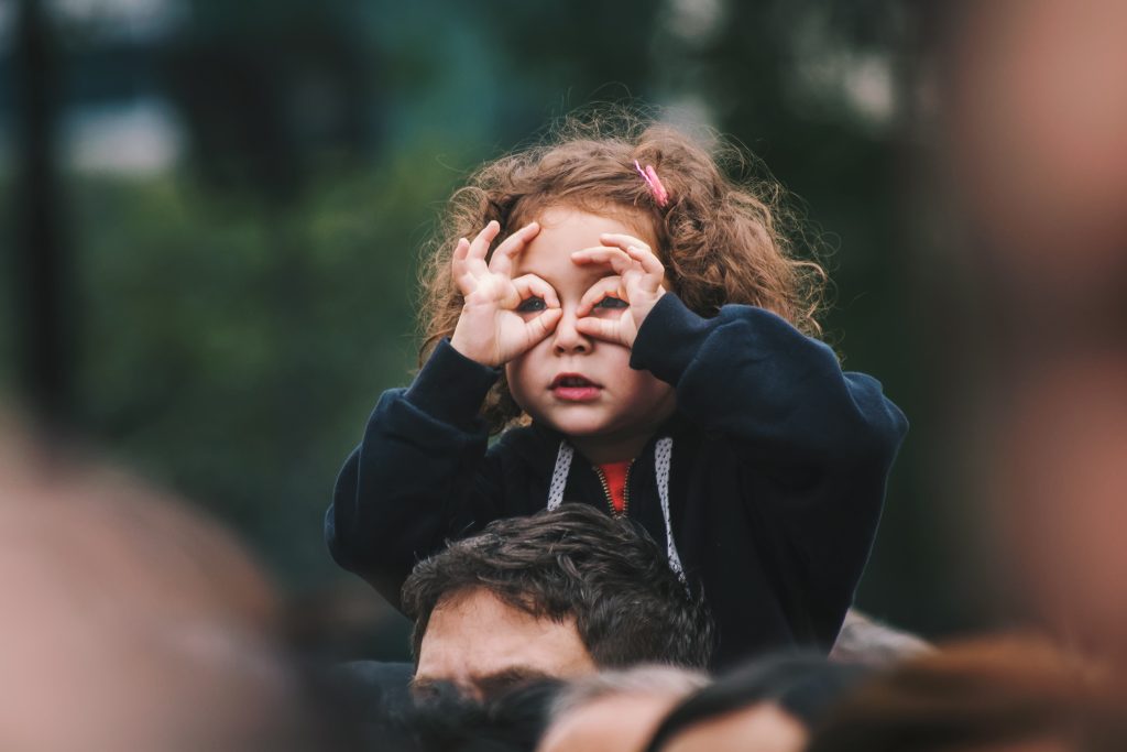 Little girl on her father's shoulders, looking through her pretend binoculars.